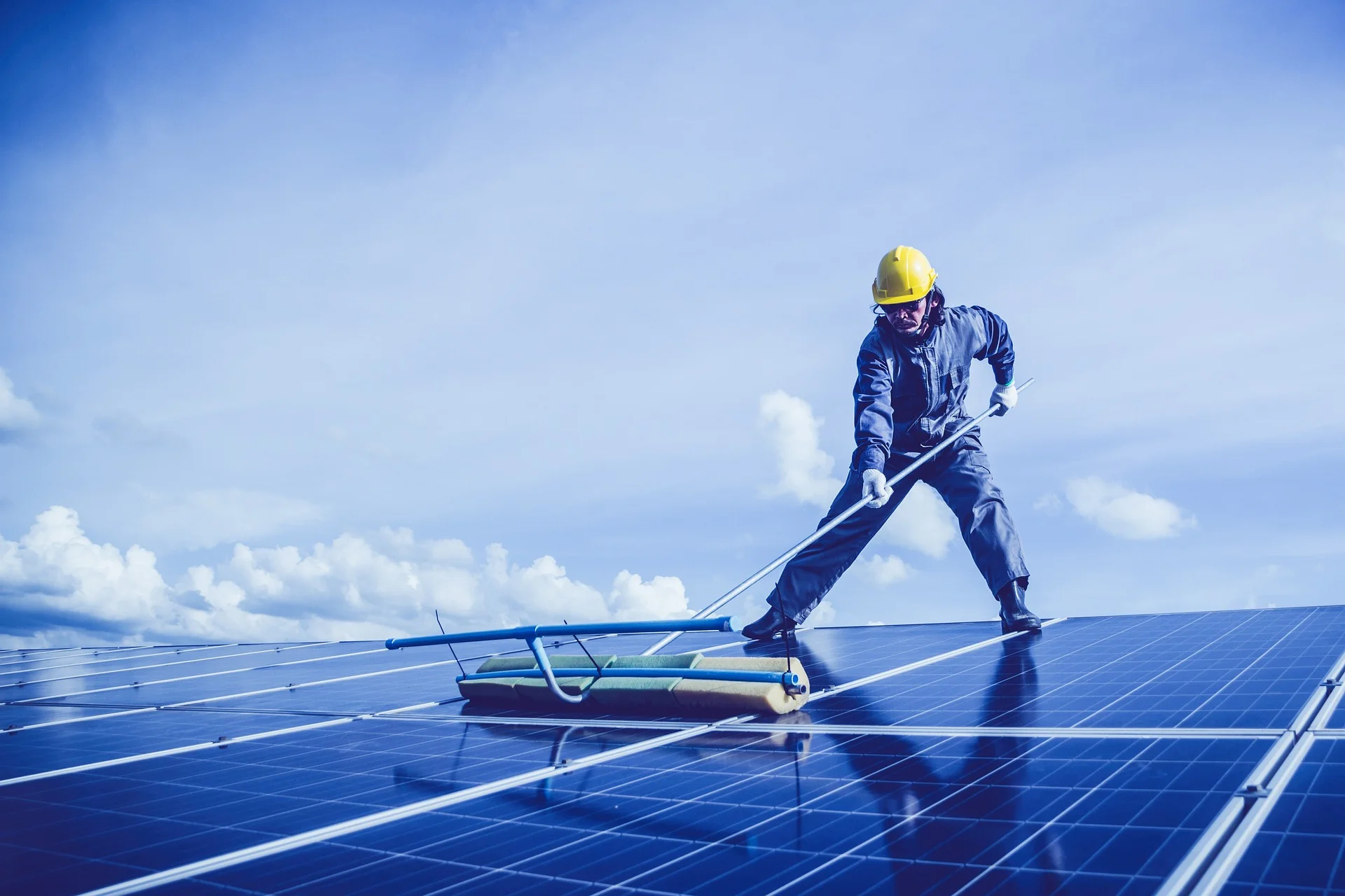 homme qui nettoie des panneaux solaires avec un balai éponge et de l'eau