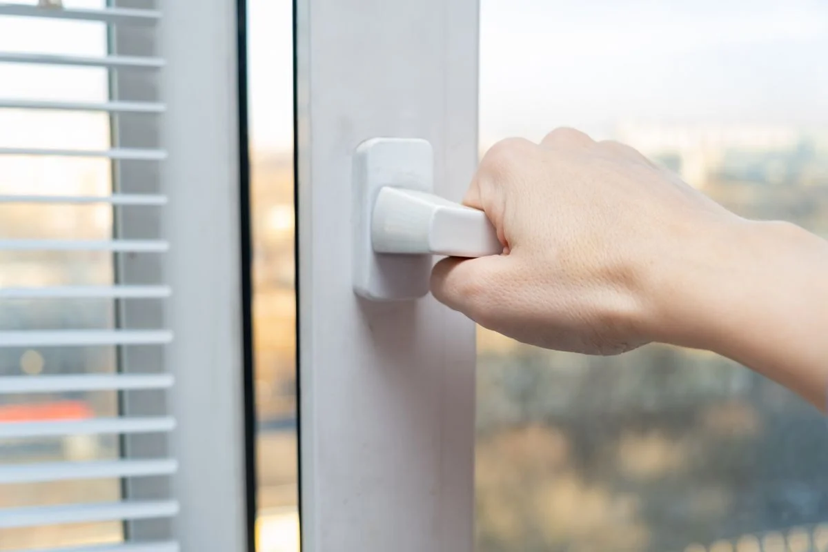 personne qui ouvre une fenêtre pour aérer son logement