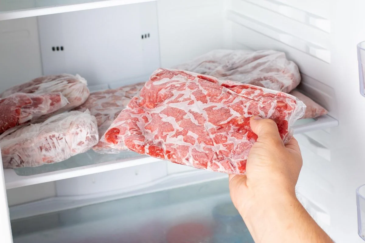 personne qui prend de viande surgelée dans son congélateur