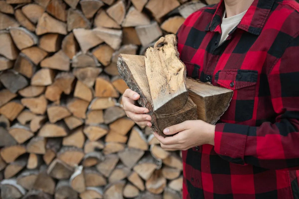 femme devant une pile de bois de chauffage qui porte des buches